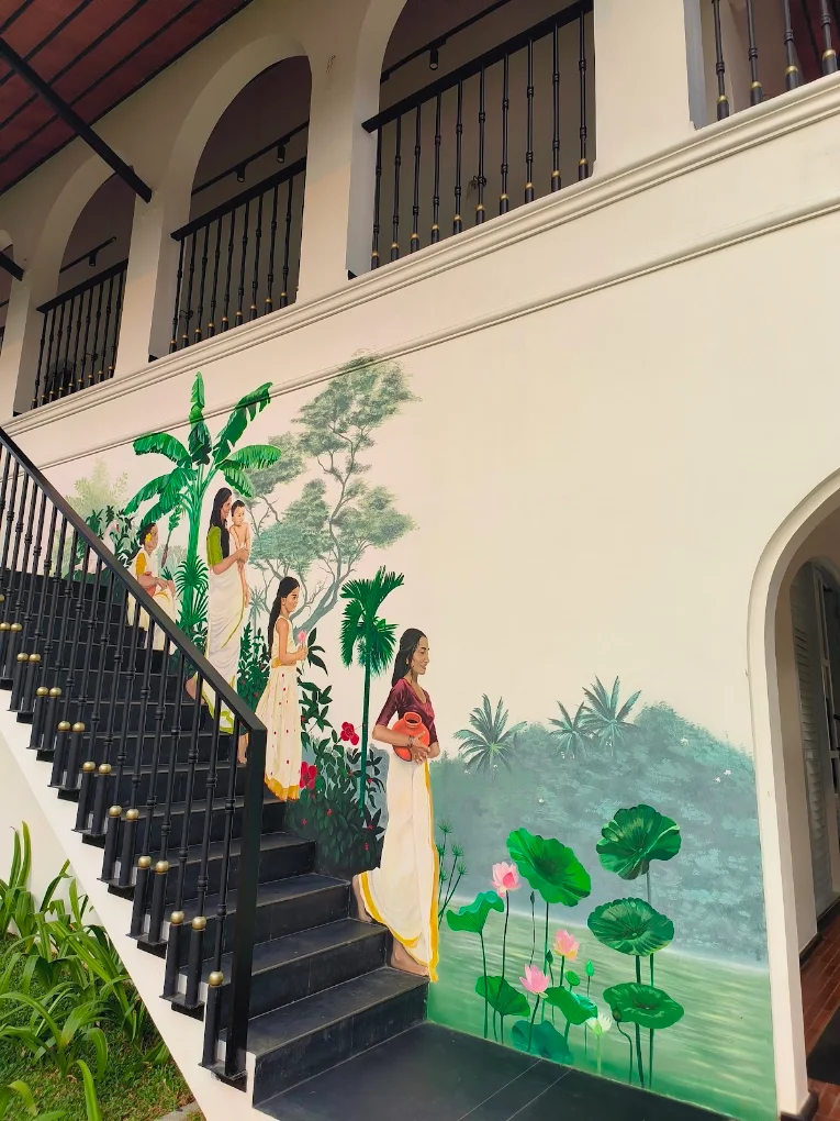 A hand-painted mural of women among lotus flowers along a staircase at One Kochi